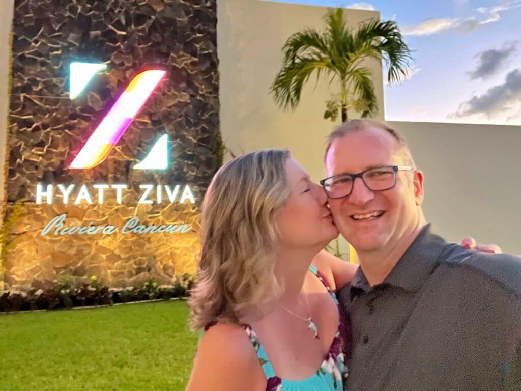 Ross getting a kiss from Zuzu in front of Hyatt Ziva Riviera Cancun All Inclusive Resort sign.