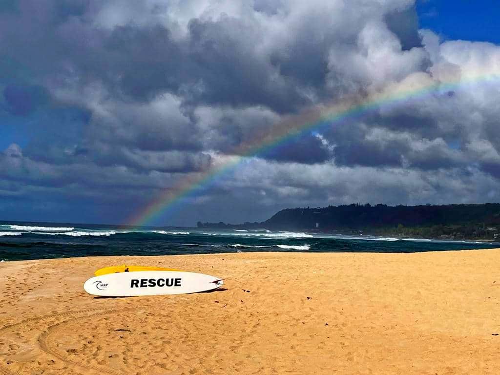 rainbow above beach in Hawaii with a lifeguard's rescue surfboard