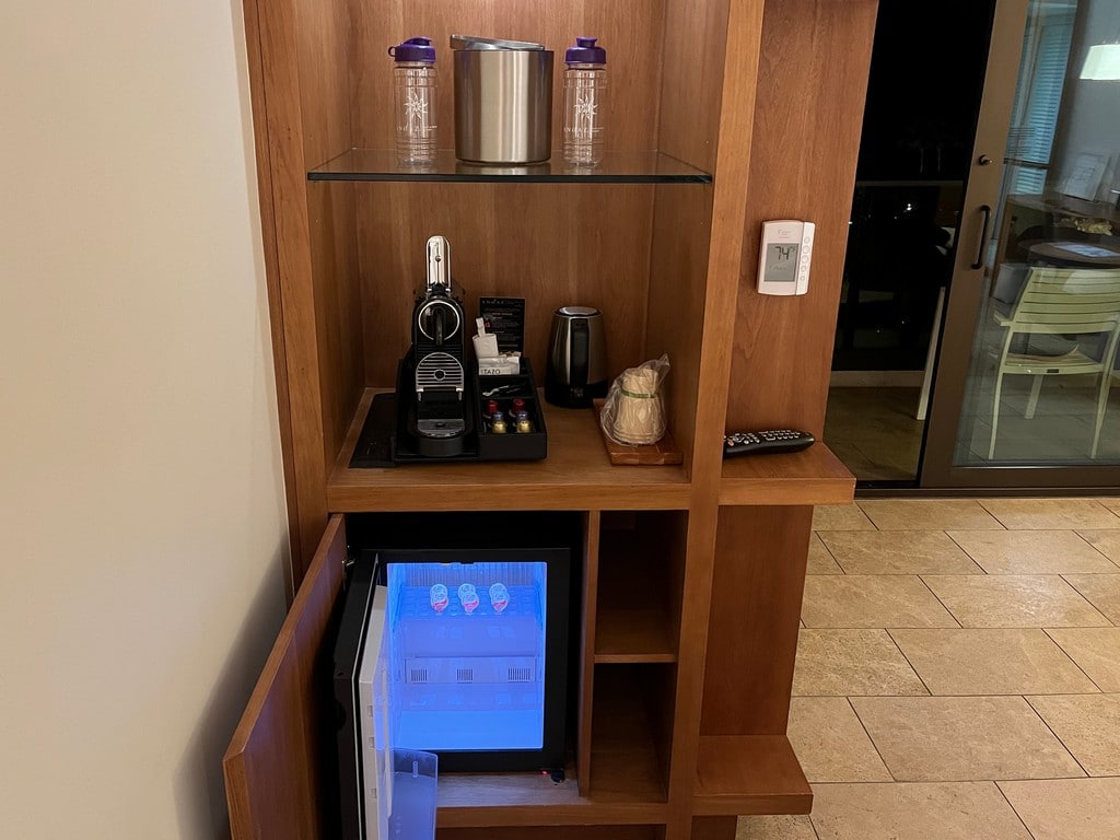 mini fridge, coffee maker and ice bucket on wood and glass cabinet with oceanfront balcony in background