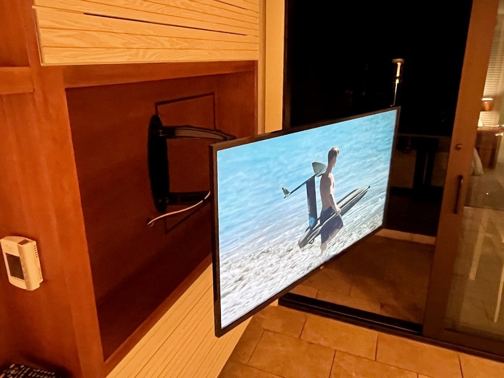 flat screen tv on pull out arm showing man with surfboard on screen