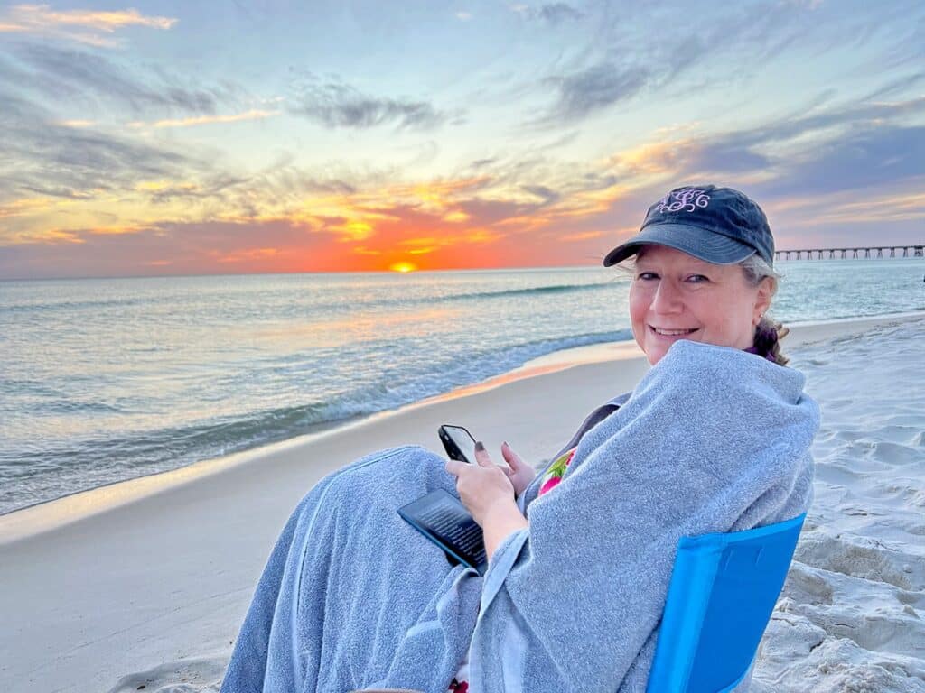 Sandra in blue cap wrapped in grey towels watching Panama City Beach sunset