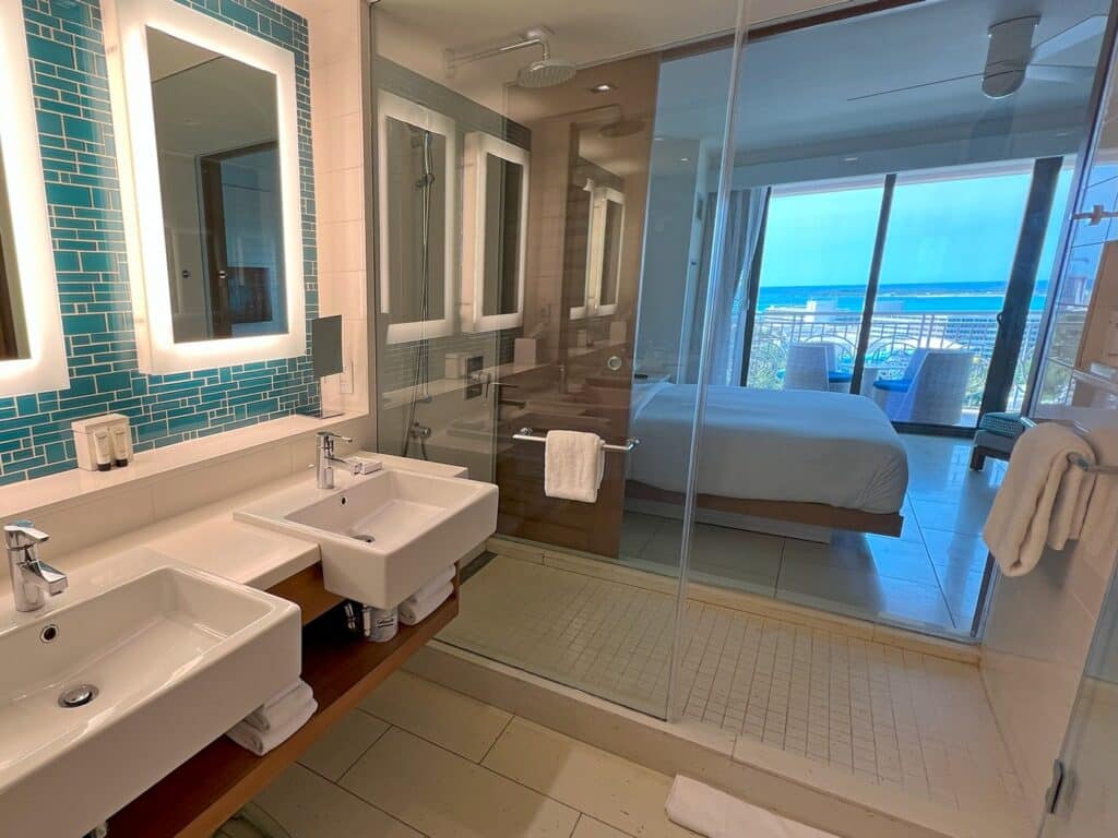 Bathroom sinks and glass shower that allows you to see the bed and ocean front balcony