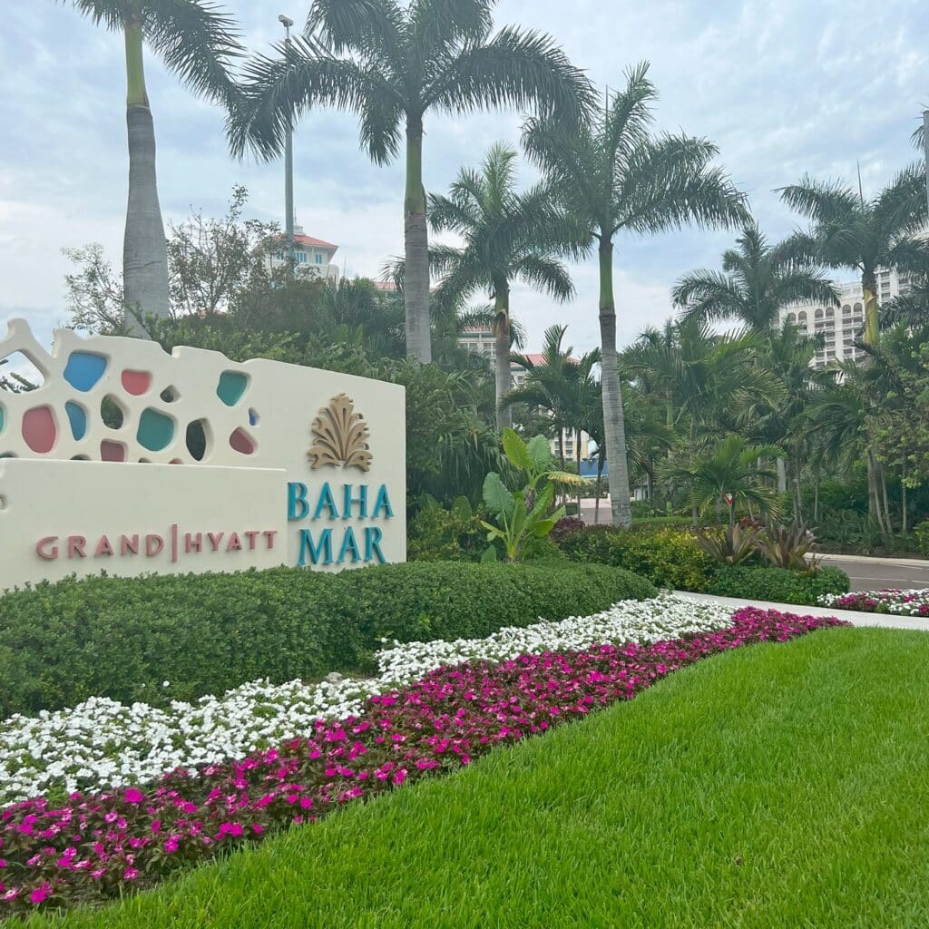 Sign for the Grand Hyatt Baha Mar surrounded by flowers and palm trees with the hotel towers in the background.