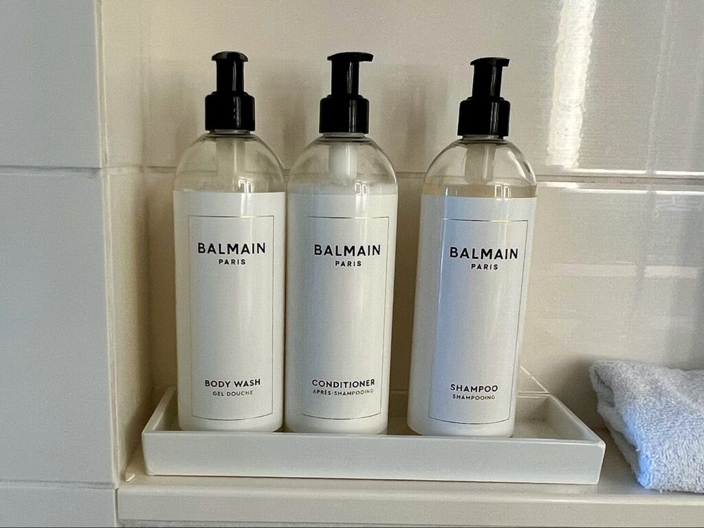 pump bottles of shampoo, conditioner and body wash from Balmain Paris in white tile bathroom