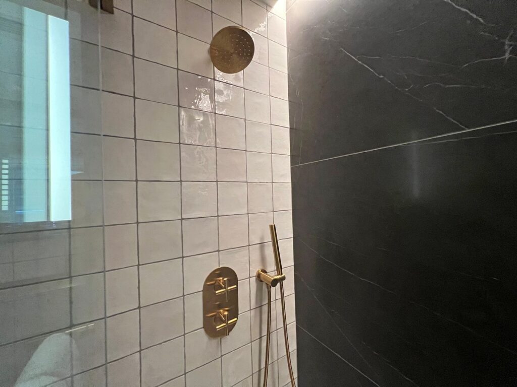 Shower with brass fixtures and white tile.