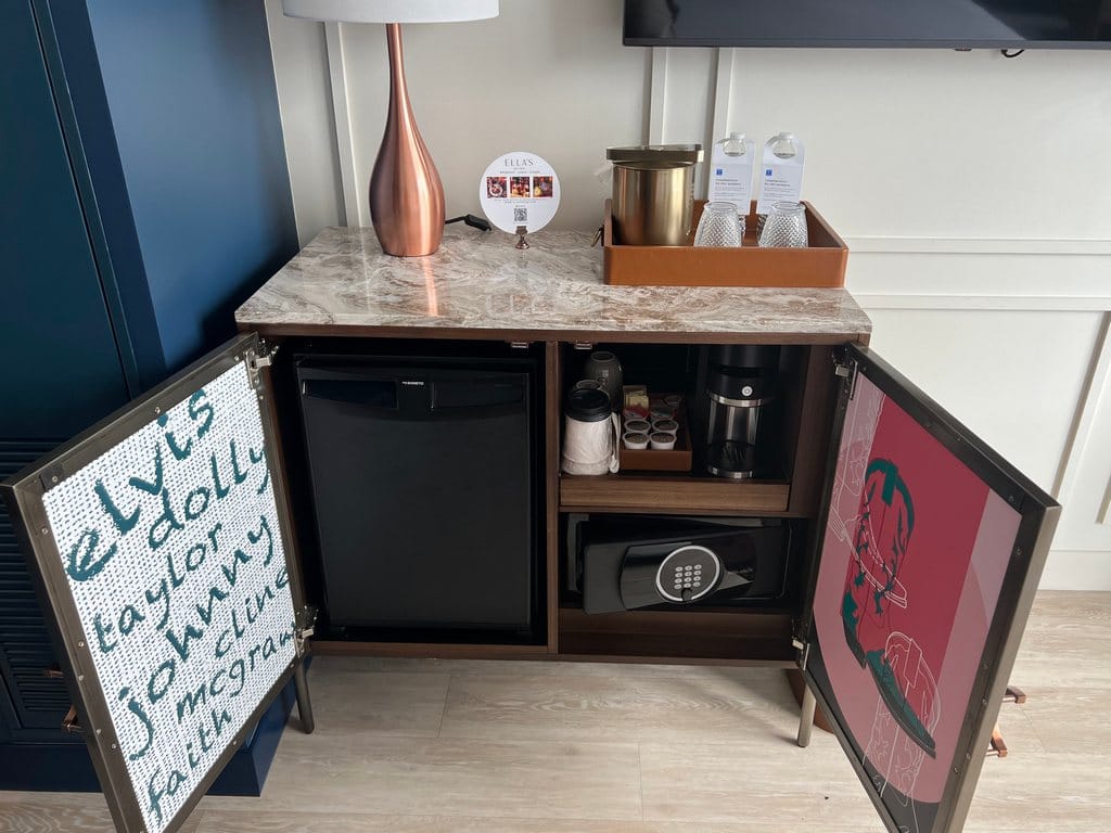 Minibar with fridge, safe, coffee maker inside and copper lamp ice bucket and glassware on top.