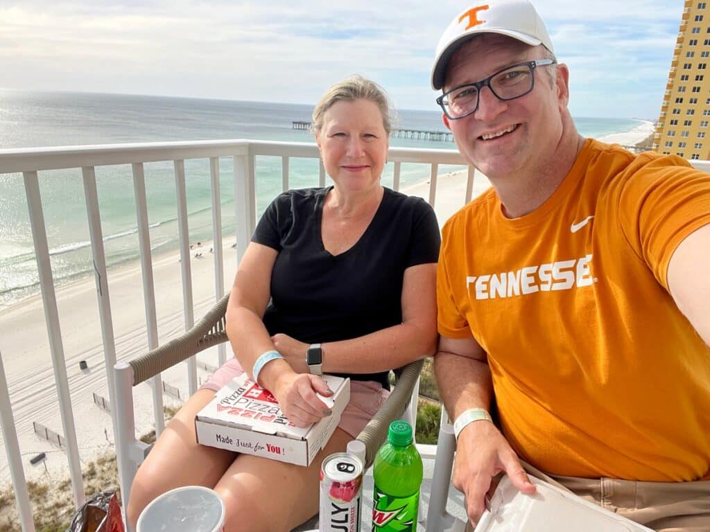 Ross & Zuzu with pizza and drinks sitting on the balcony with PCB and Gulf of Mexico in the background.