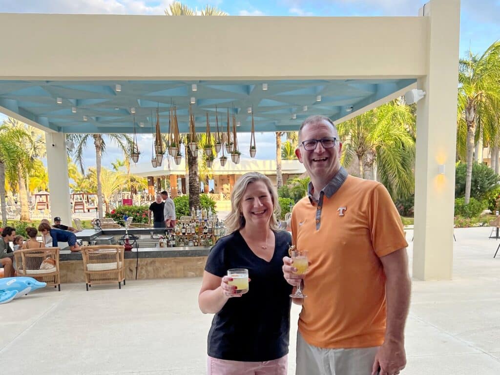Ross & Sandra with free drinks at the Hyatt Ziva Riviera Cancun bar in front of  palm trees