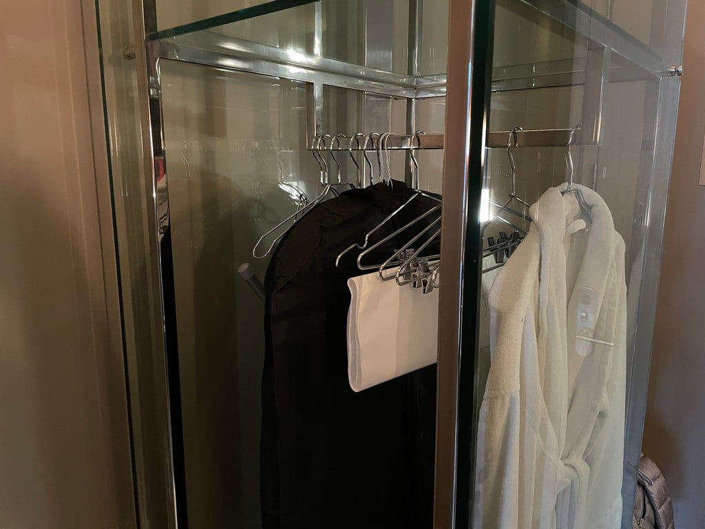glass and chrome closet with hangers and a white robe in our Andaz hotel room