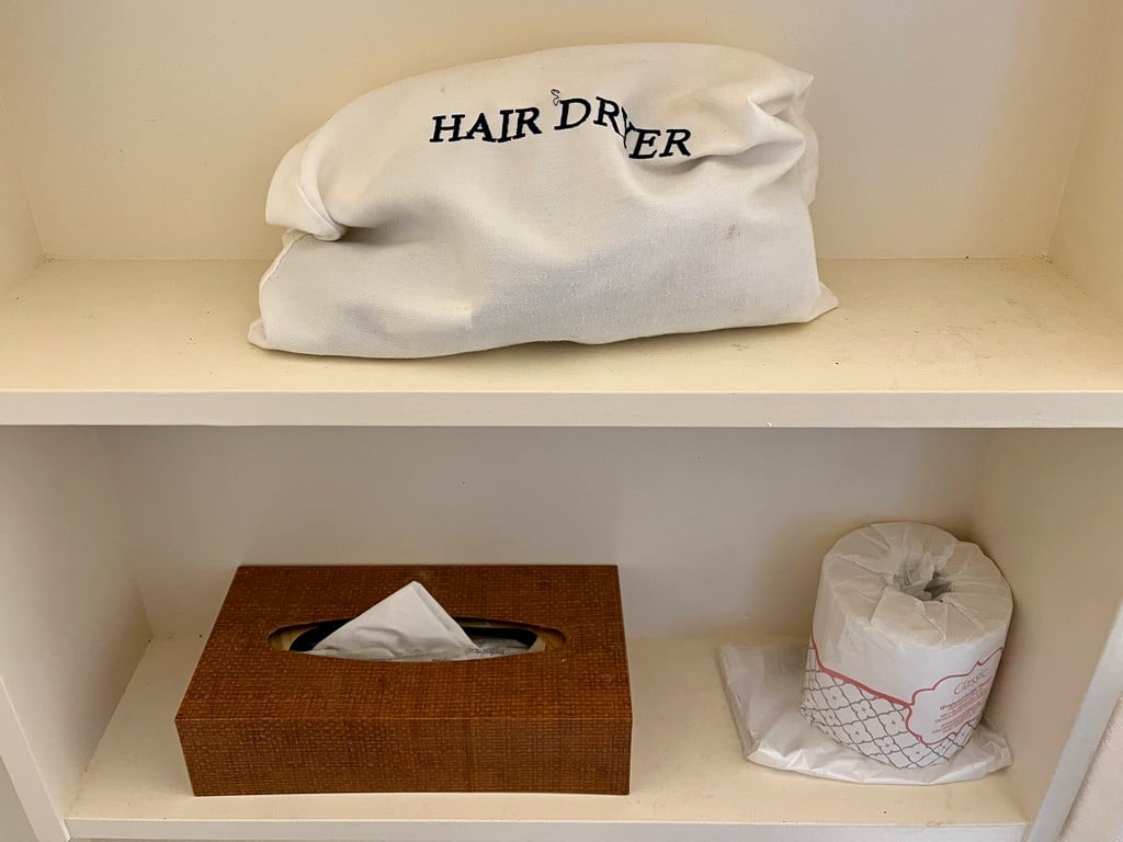 Hair dryer in a bag, a box of tissues and a roll of toilet paper in the Volcano House Hotel room's bathroom.