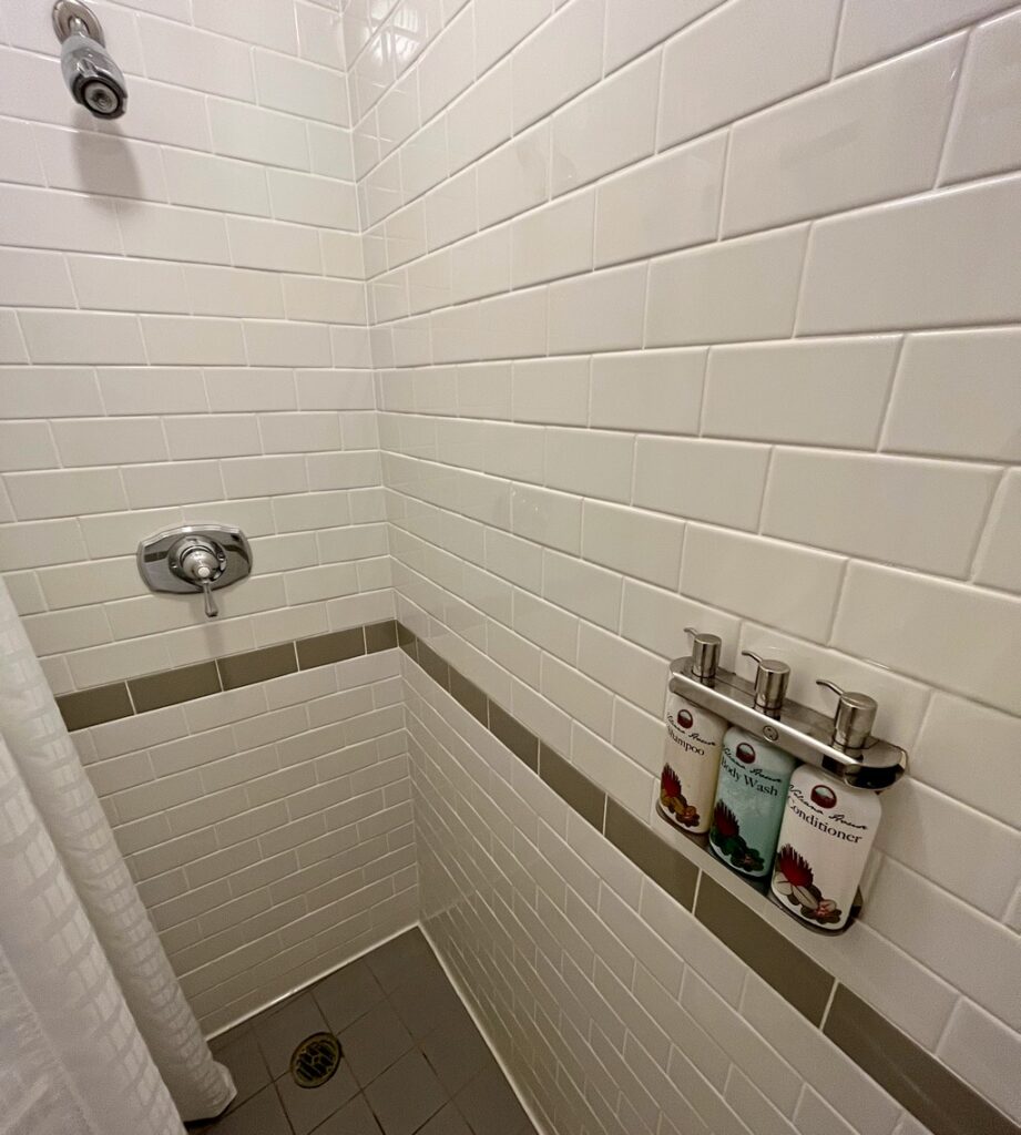 white tile shower stall with pump bottles of shampoo, conditioner and body lotion