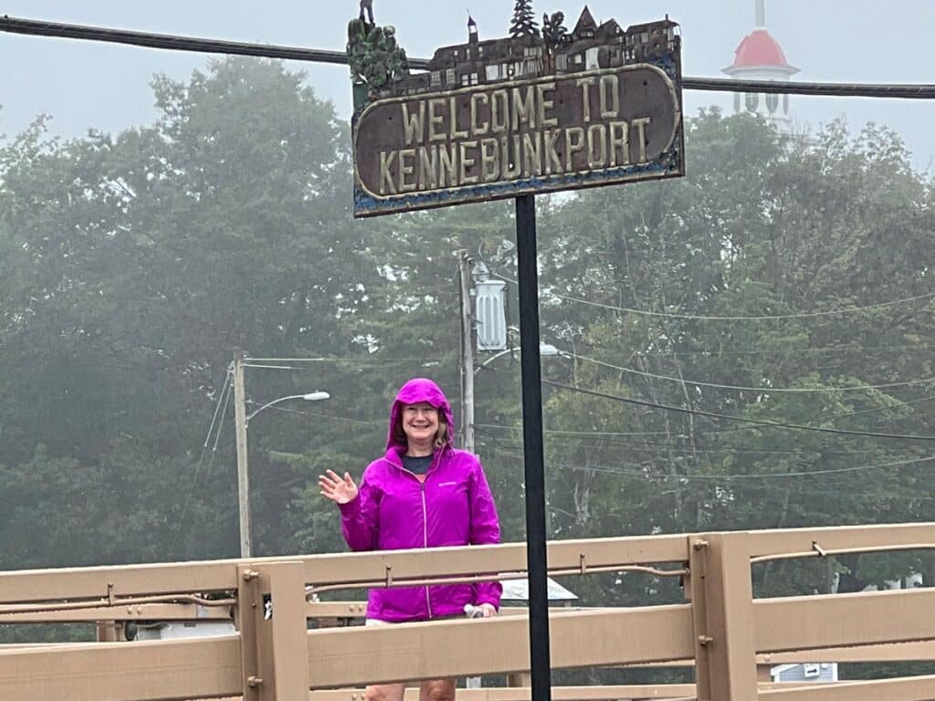 Zuzu waving in front of Welcome to Kennebunkport sign